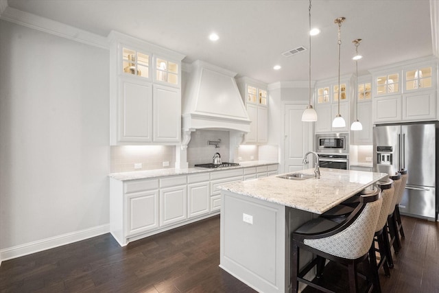 kitchen featuring white cabinetry, appliances with stainless steel finishes, a kitchen island with sink, light stone countertops, and wall chimney range hood