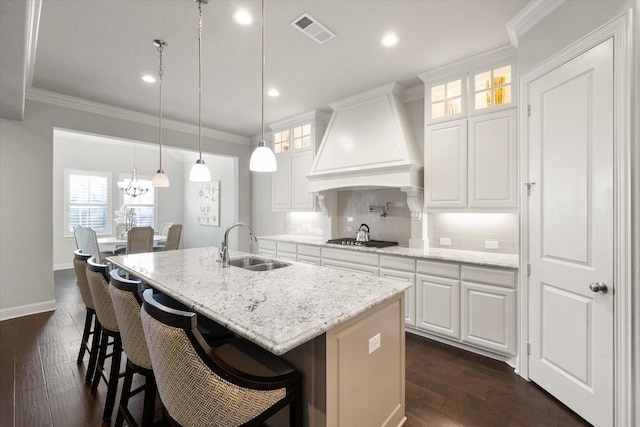 kitchen with premium range hood, sink, white cabinets, and an island with sink