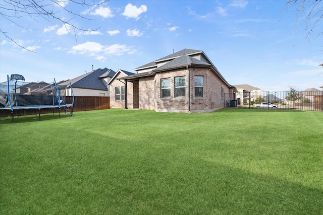 rear view of house with a trampoline, cooling unit, and a lawn