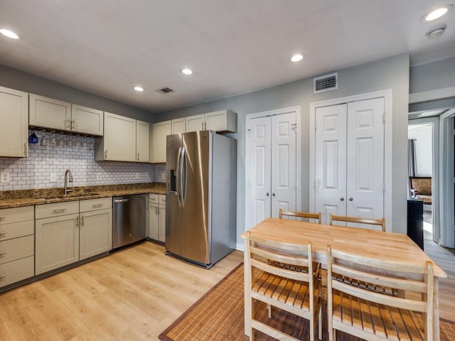 kitchen with appliances with stainless steel finishes, dark stone countertops, tasteful backsplash, sink, and light hardwood / wood-style flooring