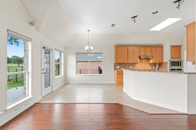 kitchen with light stone counters, stainless steel microwave, hanging light fixtures, a notable chandelier, and tasteful backsplash