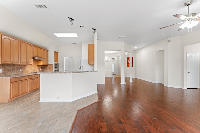 kitchen featuring stainless steel appliances, light stone counters, kitchen peninsula, ceiling fan with notable chandelier, and decorative backsplash