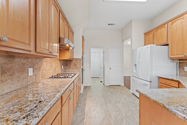 kitchen with white refrigerator with ice dispenser, stainless steel gas cooktop, light stone countertops, wall chimney range hood, and backsplash