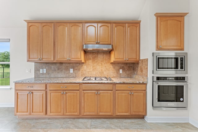 kitchen with stainless steel appliances, decorative backsplash, vaulted ceiling, and light stone countertops