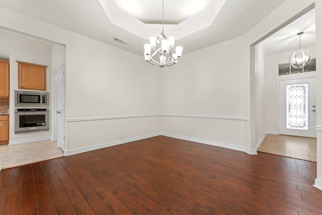 interior space featuring hardwood / wood-style flooring, a raised ceiling, a notable chandelier, and ornamental molding