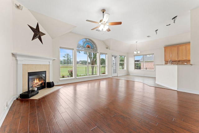 unfurnished living room with ceiling fan with notable chandelier, a fireplace, vaulted ceiling, and light hardwood / wood-style floors