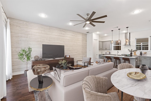 living room with ceiling fan, wooden walls, dark hardwood / wood-style floors, and sink