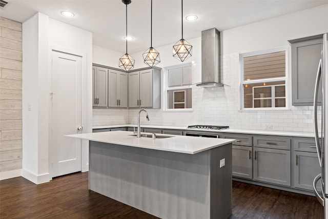 kitchen featuring sink, decorative light fixtures, wall chimney exhaust hood, an island with sink, and dark hardwood / wood-style flooring