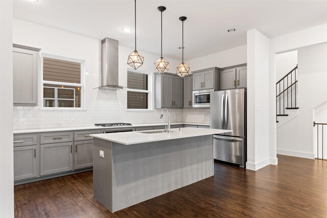 kitchen featuring a kitchen island with sink, stainless steel appliances, hanging light fixtures, sink, and range hood