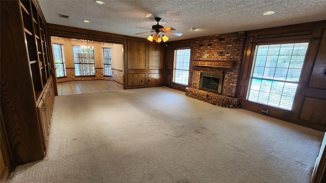 unfurnished living room with a brick fireplace, light colored carpet, ceiling fan, and a textured ceiling