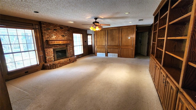 unfurnished living room with ceiling fan, a brick fireplace, light carpet, and a textured ceiling