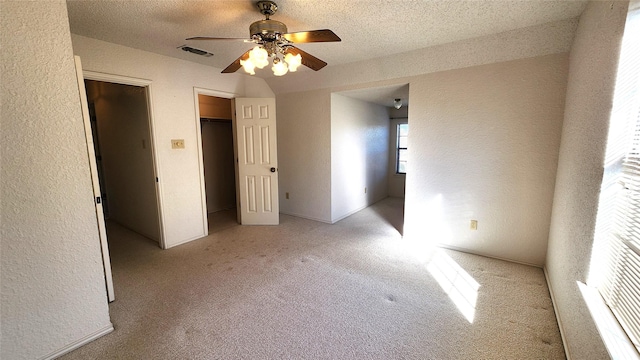 unfurnished bedroom featuring a walk in closet, a textured ceiling, ceiling fan, and light carpet