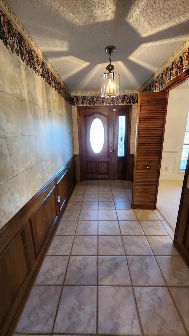 tiled entrance foyer featuring a textured ceiling and a chandelier