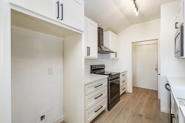 kitchen featuring wall chimney range hood, appliances with stainless steel finishes, white cabinets, decorative backsplash, and vaulted ceiling