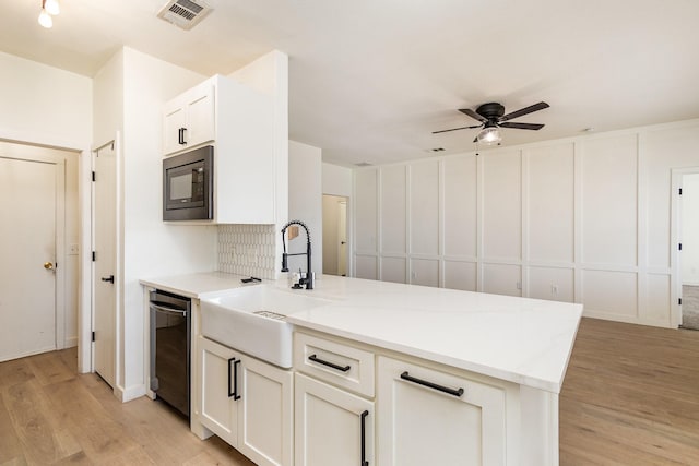 kitchen with built in microwave, sink, light wood-type flooring, black dishwasher, and white cabinets