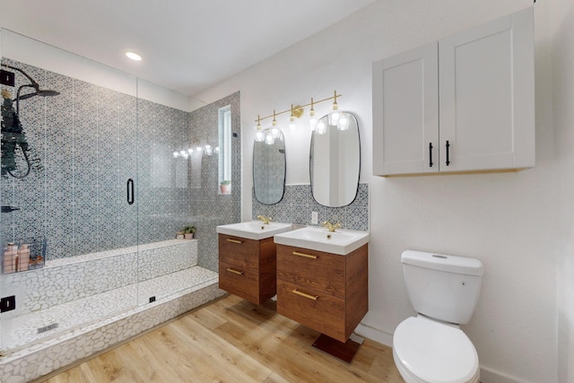 bathroom with hardwood / wood-style floors, toilet, vanity, a shower with shower door, and backsplash