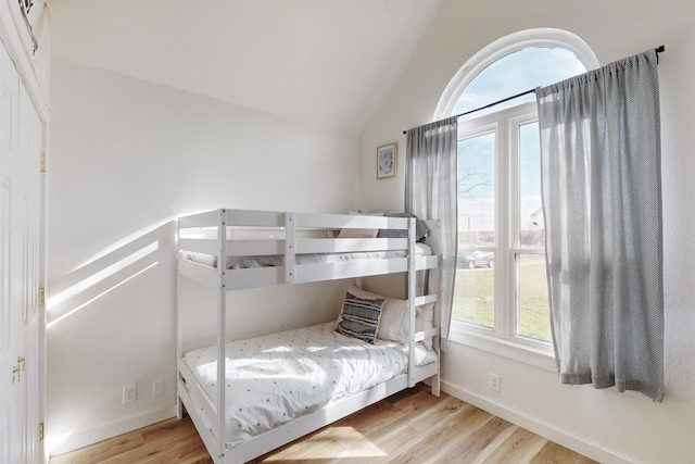 bedroom featuring multiple windows, light wood-type flooring, and vaulted ceiling