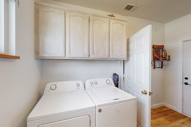 washroom featuring cabinets, washing machine and dryer, and light wood-type flooring