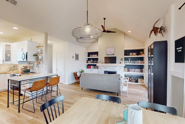 living room featuring light wood-type flooring, ceiling fan, built in features, a premium fireplace, and high vaulted ceiling