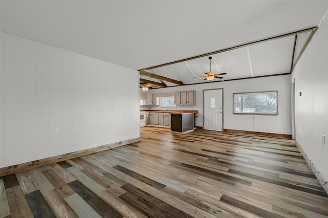 unfurnished living room with sink, lofted ceiling with beams, ceiling fan, and light hardwood / wood-style flooring