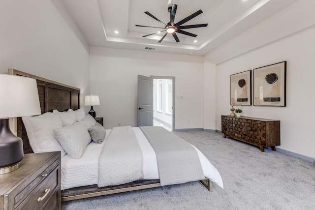 carpeted bedroom with ceiling fan and a tray ceiling