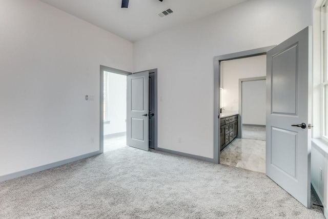 unfurnished bedroom featuring ceiling fan, ensuite bathroom, and light carpet