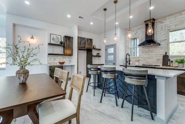 kitchen featuring sink, decorative light fixtures, wall chimney exhaust hood, decorative backsplash, and a breakfast bar