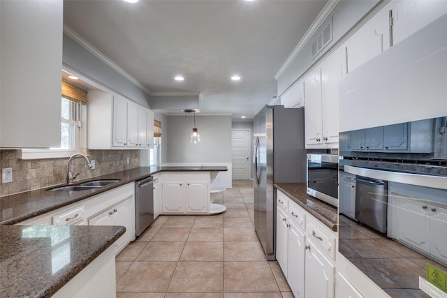 kitchen with hanging light fixtures, stainless steel appliances, white cabinetry, dark stone countertops, and sink