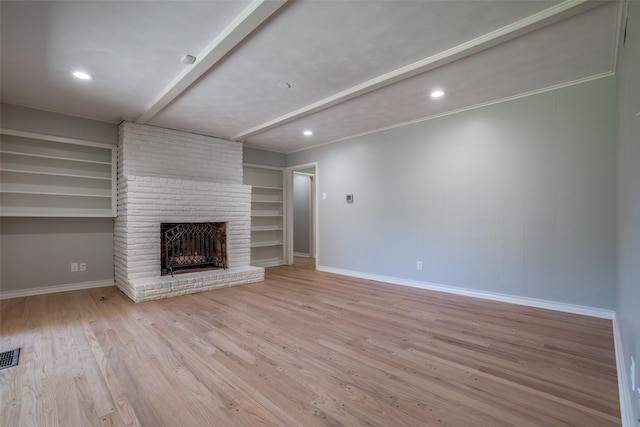 unfurnished living room featuring beamed ceiling, ornamental molding, light wood-type flooring, a brick fireplace, and built in shelves