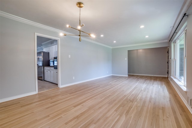 spare room with an inviting chandelier, light hardwood / wood-style floors, and crown molding