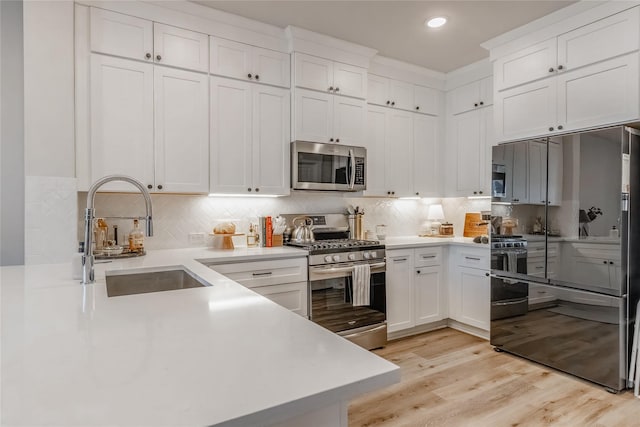 kitchen featuring appliances with stainless steel finishes, sink, white cabinets, backsplash, and light hardwood / wood-style flooring