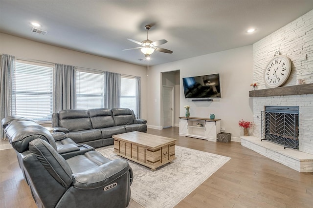 living room featuring hardwood / wood-style floors, ceiling fan, and a stone fireplace