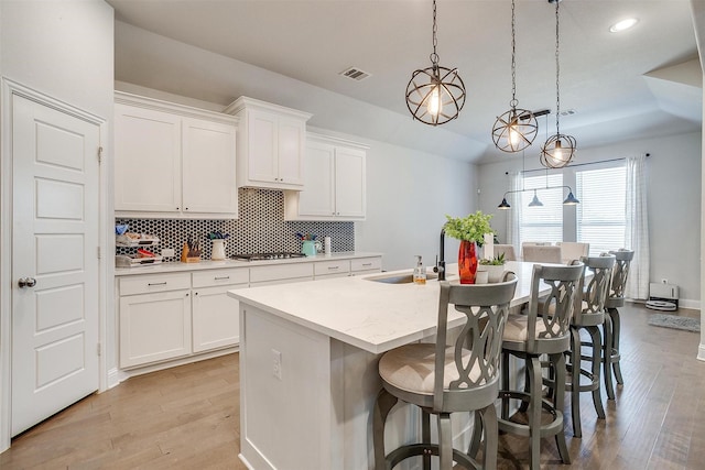 kitchen featuring an island with sink, stainless steel gas stovetop, pendant lighting, and white cabinetry