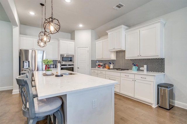 kitchen with a center island with sink, appliances with stainless steel finishes, pendant lighting, white cabinets, and sink