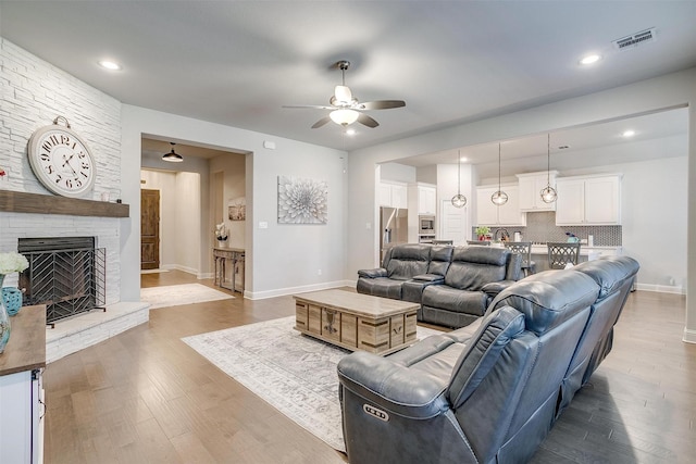 living room with ceiling fan, wood-type flooring, and a stone fireplace