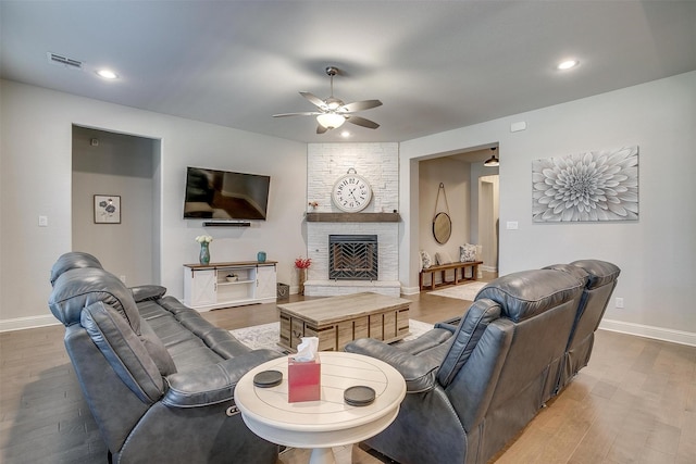 living room with a stone fireplace, ceiling fan, and hardwood / wood-style floors