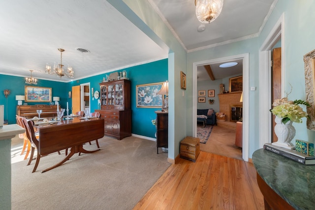 dining room featuring a fireplace, light wood-type flooring, crown molding, and an inviting chandelier