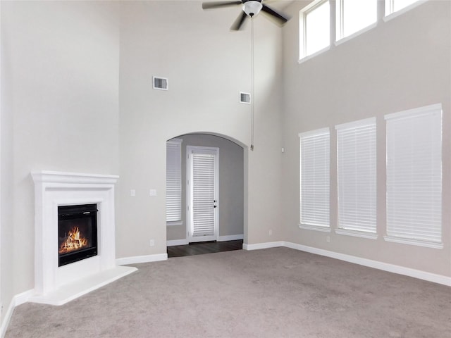 unfurnished living room with a high ceiling, light carpet, and ceiling fan