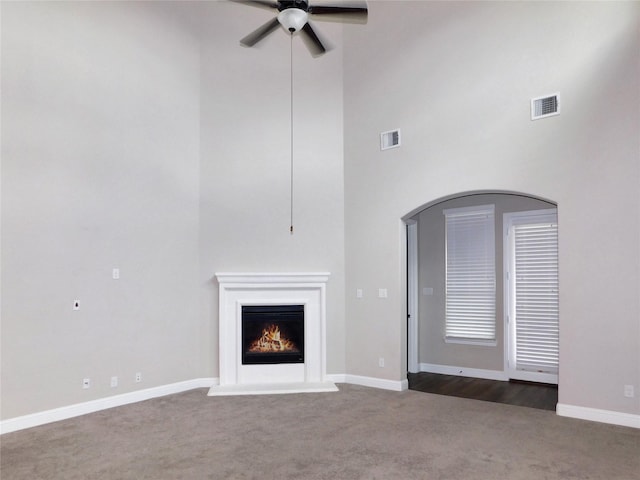 unfurnished living room featuring a towering ceiling, ceiling fan, and dark carpet