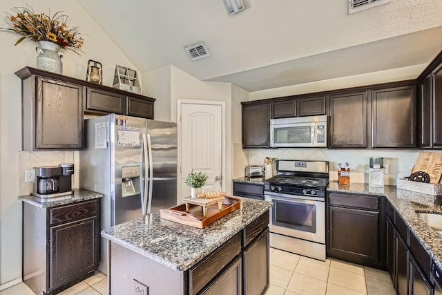 kitchen featuring a center island, lofted ceiling, stone countertops, backsplash, and appliances with stainless steel finishes