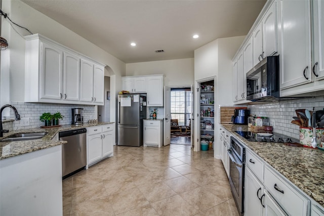 kitchen featuring light stone counters, stainless steel appliances, decorative backsplash, white cabinets, and sink