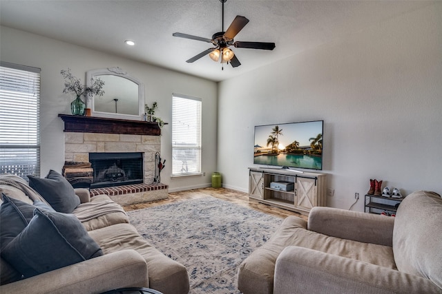 living room with ceiling fan, light hardwood / wood-style flooring, a stone fireplace, and a textured ceiling