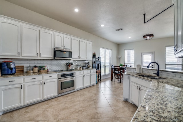 kitchen with sink, stainless steel oven, white cabinetry, light stone counters, and decorative backsplash