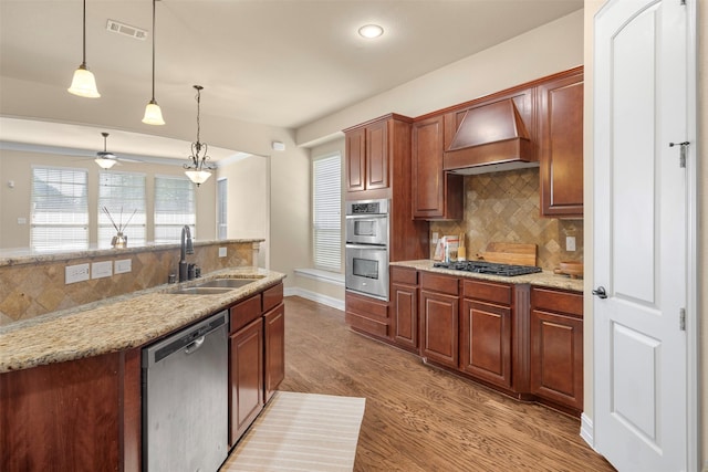 kitchen with light stone counters, custom exhaust hood, decorative light fixtures, stainless steel appliances, and sink