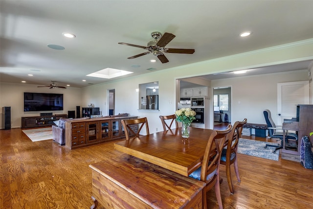 dining space featuring wood-type flooring, ceiling fan, crown molding, and a skylight