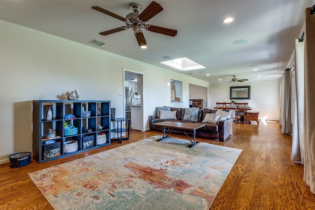 living room featuring crown molding, hardwood / wood-style floors, ceiling fan, and a skylight