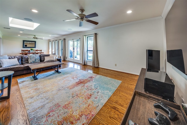 living room with ceiling fan, a skylight, ornamental molding, and wood-type flooring