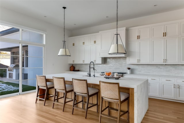 kitchen with tasteful backsplash, light wood-type flooring, a kitchen island with sink, white cabinets, and sink