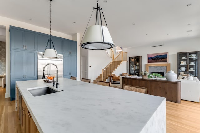 kitchen featuring a center island with sink, blue cabinetry, pendant lighting, sink, and light hardwood / wood-style flooring