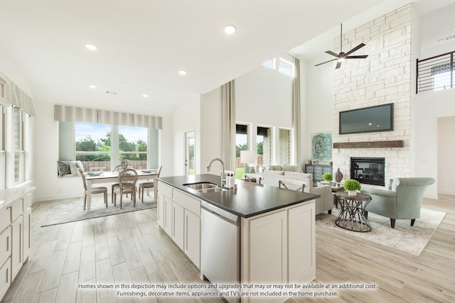 kitchen with plenty of natural light, a fireplace, white cabinets, stainless steel dishwasher, and sink